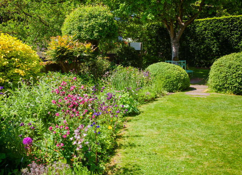 Green summer walled english formal garden with lawn blooming flowers and hedgerow in background, Southern England, UK